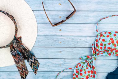 Mavi ahşap bir arka planda duran, gözlüklü, beyaz şapkalı ve mayosu olan saman rengi bir adam..