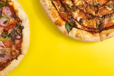 Sarı arka planda iki farklı lezzetli büyük pizza..