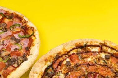 Sarı arka planda iki farklı lezzetli büyük pizza..