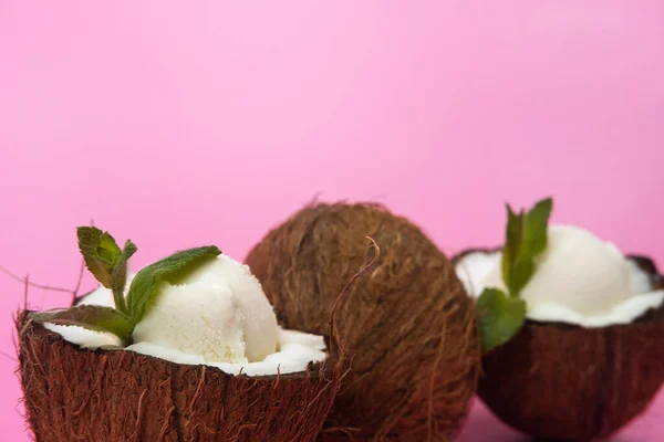 ピンクの背景にミントの葉で飾られた新鮮なココナッツの半分にバニラアイスボール — ストック写真