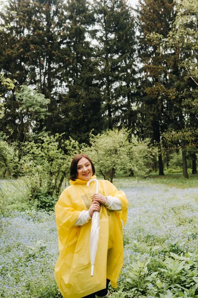 a woman in a yellow raincoat walks in the park and garden in the summer.