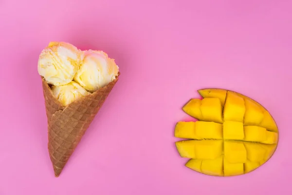 Mango-flavored ice cream balls in a waffle cone on a pink background. Ripe mango with ice cream on a pink background