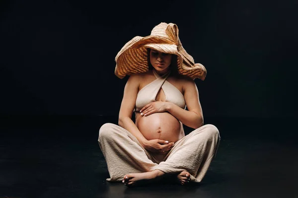 Una Mujer Embarazada Sombrero Paja Sienta Suelo Ropa Beige Estudio — Foto de Stock