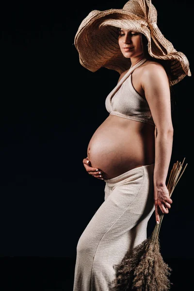 Беременная Женщина Соломенной Шляпе Бежевой Одеждой Букетом Руках Студии Черном — стоковое фото