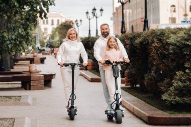 Beyaz elbiseli bir aile şehirde elektrikli scooter kullanıyor. Açık hava aktiviteleri..