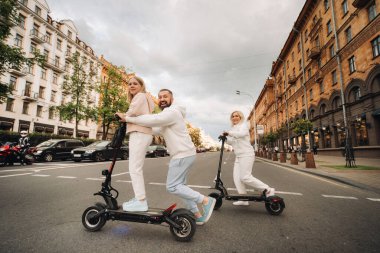 Beyaz elbiseli bir aile şehirde elektrikli scooter kullanıyor. Açık hava aktiviteleri..