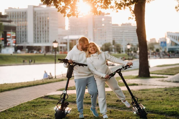Beyaz Elbiseli Bir Çift Gün Batımında Elektrikli Scooterlarla Şehirde Duruyor — Stok fotoğraf