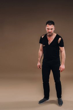 Gri arka planda siyah tişörtlü hırpalanmış bir adam duruyor..