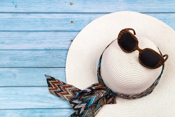 Mavi ahşap bir arka planda duran gözlüklü samandan beyaz şapkanın üst görüntüsü..