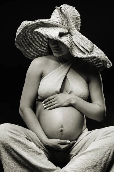妊娠中の女性が黒い背景のスタジオでベージュの服を着て床に座っています — ストック写真
