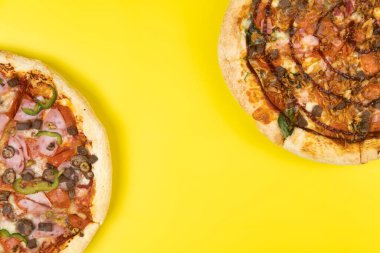 Sarı arka planda iki farklı lezzetli büyük pizza..