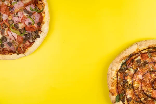 Sarı arka planda iki farklı lezzetli büyük pizza..