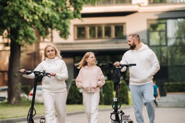 Beyaz elbiseli bir aile şehirde elektrikli scooter kullanıyor. Açık hava aktiviteleri..