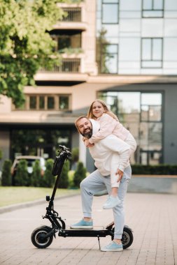 Beyaz elbiseli bir aile şehirde elektrikli scooterla duruyor. Baba ve kızı elektrikli scooterda.