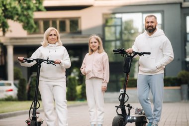 Beyaz elbiseli bir aile şehirde elektrikli scooter kullanıyor. Açık hava aktiviteleri.
