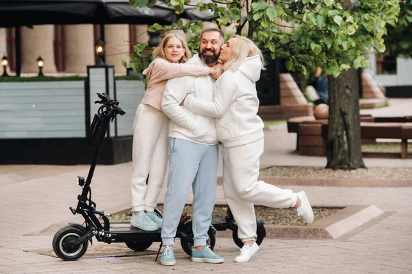 Una familia de ropa blanca se para en la ciudad en scooters eléctricos — Foto de Stock