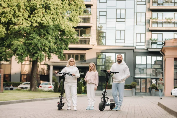 A család fehér ruhás lovagol elektromos robogók a városban.Kültéri tevékenységek — Stock Fotó