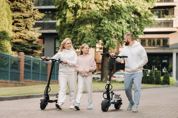 A család fehér ruhás lovagol elektromos robogók a városban.Kültéri tevékenységek — Stock Fotó