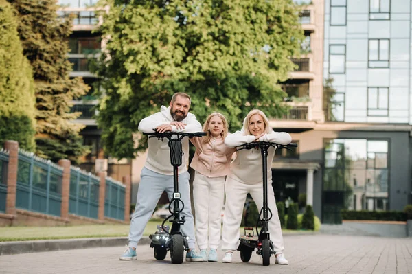 Egy fehér ruhás család áll a városban elektromos robogókon. — Stock Fotó