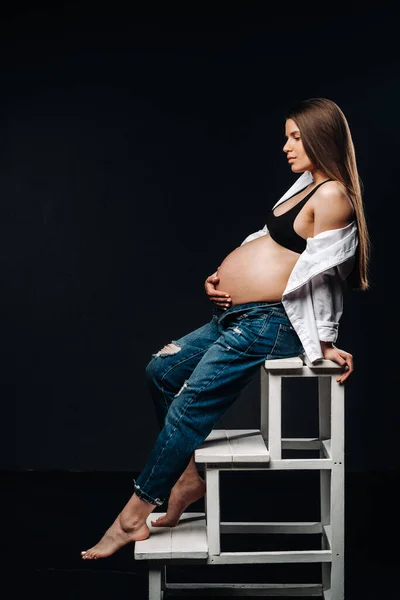 妊娠中の女性は黒い背景のスタジオではしごの椅子に座って — ストック写真