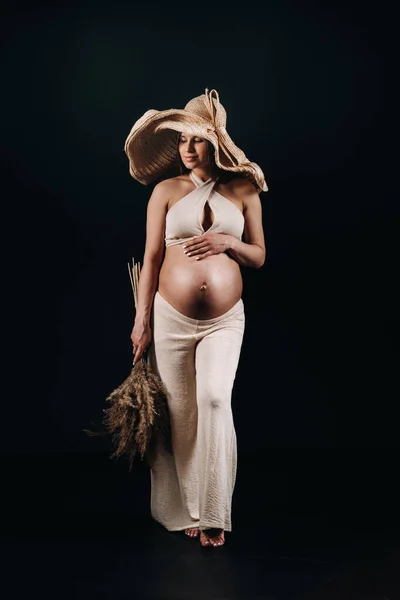 Беременная Женщина Соломенной Шляпе Бежевой Одеждой Букетом Руках Студии Черном — стоковое фото
