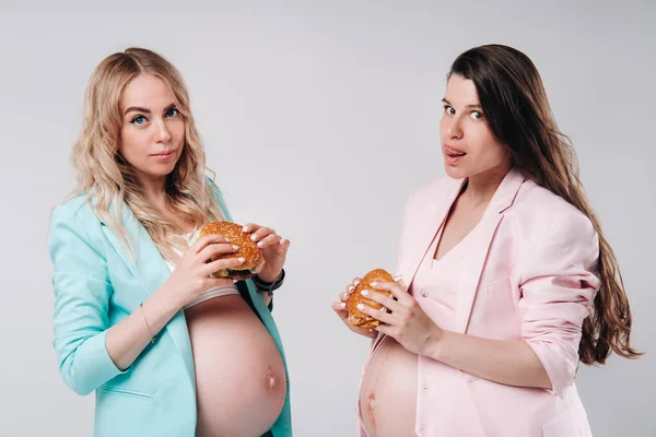 2人の妊婦スーツでハンバーガーと彼らの手に灰色の背景 — ストック写真