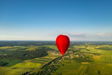 Yeşil tarlalar ve ormanların üzerinde insanların olduğu kırmızı kalp şeklinde bir balon..