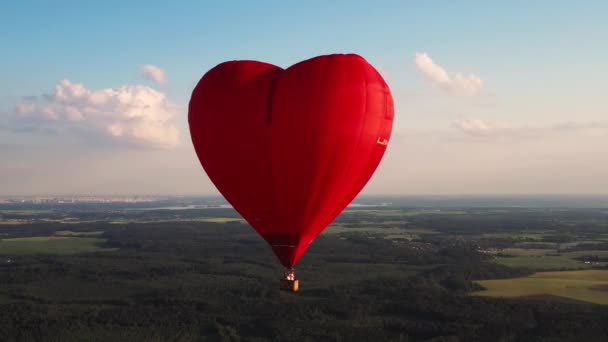 Roter herzförmiger Ballon mit Menschen über grüne Felder und Wälder — Stockvideo