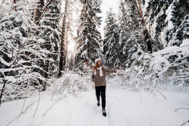 Süveter ve gözlüklü bir kız kışın karla kaplı ormanda yürür..