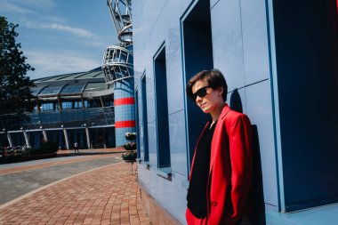 Kırmızı elbiseli bir kız şehrin modern binasının arka planında duruyor..