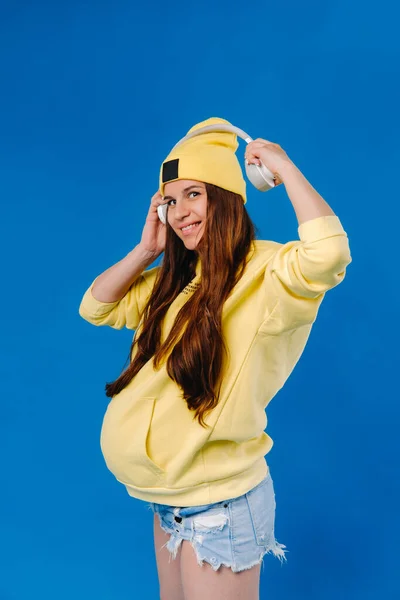 Pregnant Girl Yellow Jacket Headphones Stands Blue Background — Stock Photo, Image