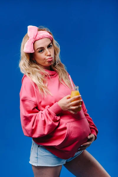 ピンクの服に青い背景にジュースが入った妊婦さん — ストック写真
