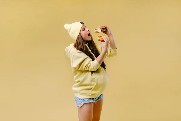 Embarazada Ropa Amarilla Con Hamburguesas Las Manos Sobre Fondo Amarillo — Foto de Stock