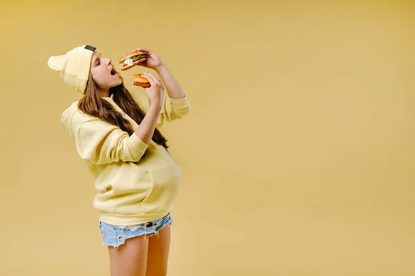 Embarazada Ropa Amarilla Con Hamburguesas Las Manos Sobre Fondo Amarillo — Foto de Stock