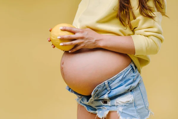 一个穿着黄色夹克的怀孕女孩站在那里 手里拿着一个黄色孤立的背景的甜瓜 — 图库照片