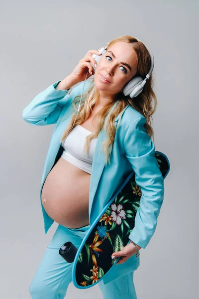 Pregnant Girl Turquoise Suit Skateboard Her Hands Headphones Stands Gray — Stock Photo, Image