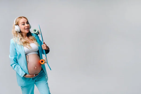 Pregnant Girl Turquoise Suit Skateboard Her Hands Headphones Stands Gray — Stock Photo, Image