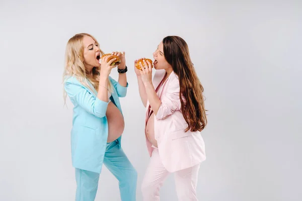 Duas Mulheres Grávidas Ternos Com Hambúrgueres Suas Mãos Fundo Cinza — Fotografia de Stock