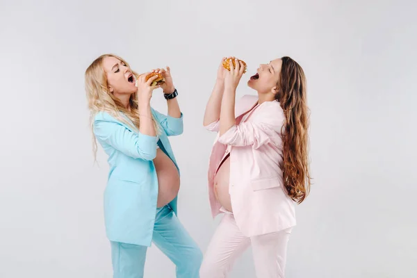 2人の妊婦スーツでハンバーガーと彼らの手に灰色の背景 — ストック写真