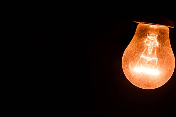Siyah arka planda bir tungsten ampulü yanıyor. Karanlık kavramda ışık. Ampul sarı ışıkla parlıyor.