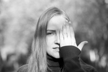 Sonbahar ağaçlarının arka planında güzel genç bir kadın. Duygu konsepti. Kız eliyle yüzünü kapatıyor..