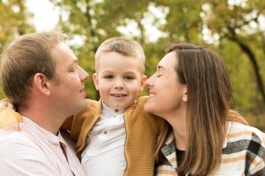 Düş! Sonbahar ormanının arka planında mutlu bir ailenin yakın çekimi. Mutlu anne, baba ve oğul gülümsüyor..