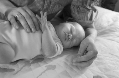 Annenin elleri bebeği dikkatlice tutuyor. Ciddi ve güzel bir bebek uyuyor. Annelik şefkati kavramı.