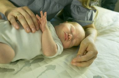 Annenin elleri bebeği dikkatlice tutuyor. Ciddi ve güzel bir bebek uyuyor. Annelik şefkati kavramı.