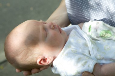 Annenin elleri bebeği dikkatlice tutuyor. Ciddi ve güzel bir bebek uyuyor. Annelik şefkati kavramı.