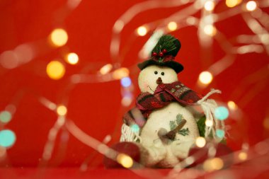 Kırmızı arka planda yeni yıl ve yılbaşı kartı. Neşeli kardan adam ve Noel ışıkları.