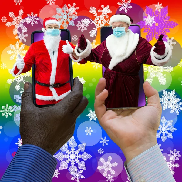 非裔美国人和白人手牵着两个圣诞老人的手机 圣诞老人戴着口罩 在带有雪花的彩虹梯度背景上的特写 — 图库照片