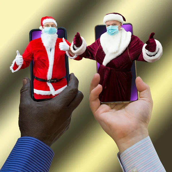 非裔美国人和白人手牵着两个圣诞老人的手机 圣诞老人戴着口罩 灰色梯度背景的特写 — 图库照片