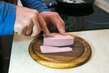 Yağlı ve sosisli omlet pişirme işlemi. Adam iki porsiyon hazırlıyor. Bir adam ahşap bir mutfak tahtasıyla sosisi parçalara ayırıyor..