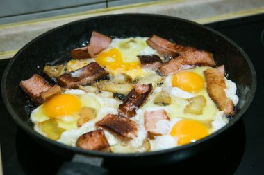 Yağlı ve sosisli omlet pişirme işlemi. Adam iki porsiyon hazırlıyor. Çırpılmış yumurtalar hazır. Kızarmış tavada domuz yağlı yumurta..